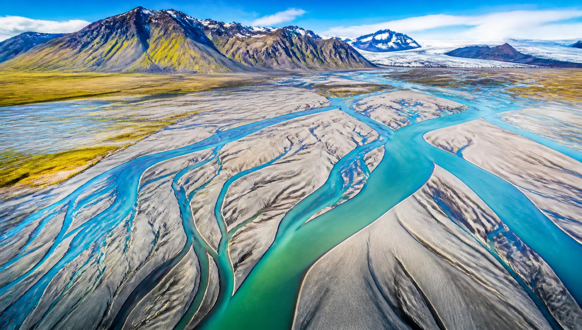 Aerial view of a steaming Icelandic geothermal valley with braided rivers and mineral-stained ground